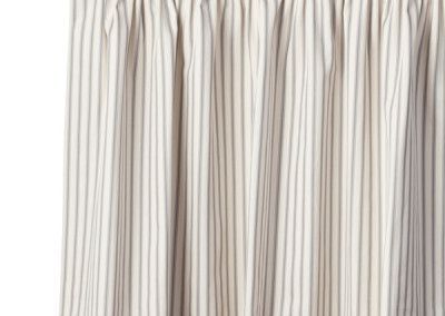 Beige and gray striped curtain hanging in front of a white background.
