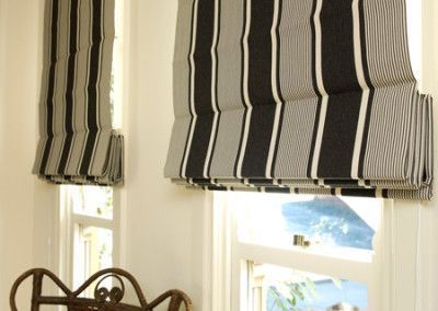 Two Roman shades with vertical black, white, and gray stripes, partially covering windows in a white room.