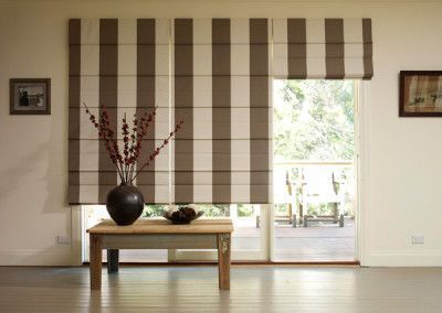 Striped Roman shades over a sliding glass door, with a table and vase in front.