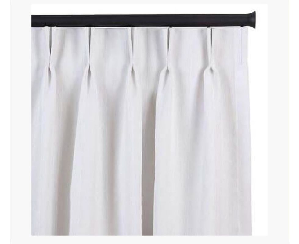White pleated curtains hanging from a black rod.