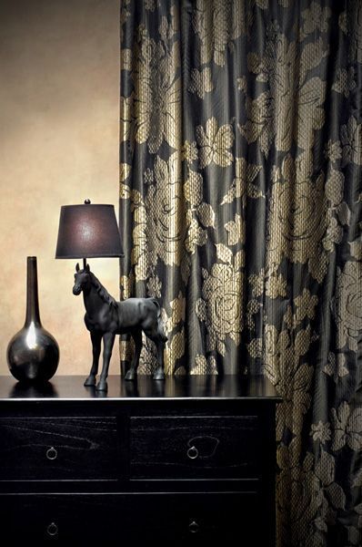 Black dresser with decor; black horse statue, lamp, vase; floral gold and black curtain.