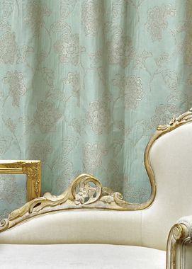 Pale green floral curtains behind a white chaise lounge with gold trim, and a small table.