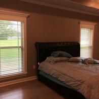 A bedroom with tan walls, light wood flooring, and a large black tufted headboard on a bed with light bedding.