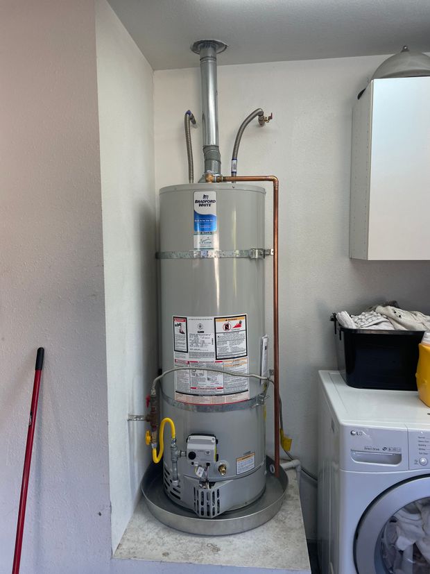 A water heater is sitting in a laundry room next to a washer and dryer.