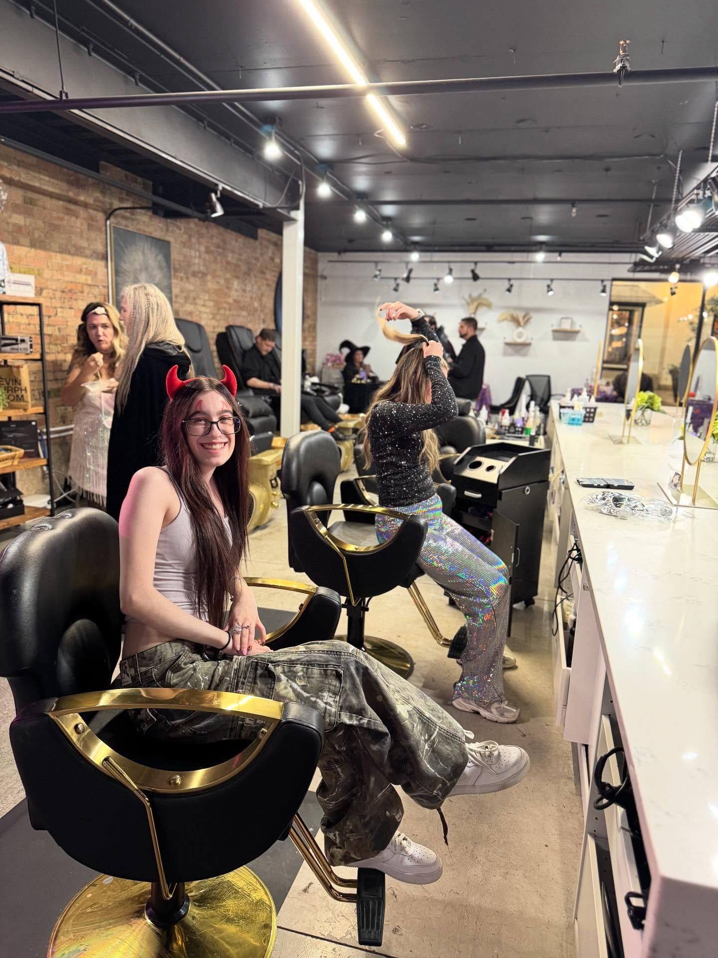 Salon with people getting hair done, mirrored styling stations, and a seated woman in a black chair in the foreground