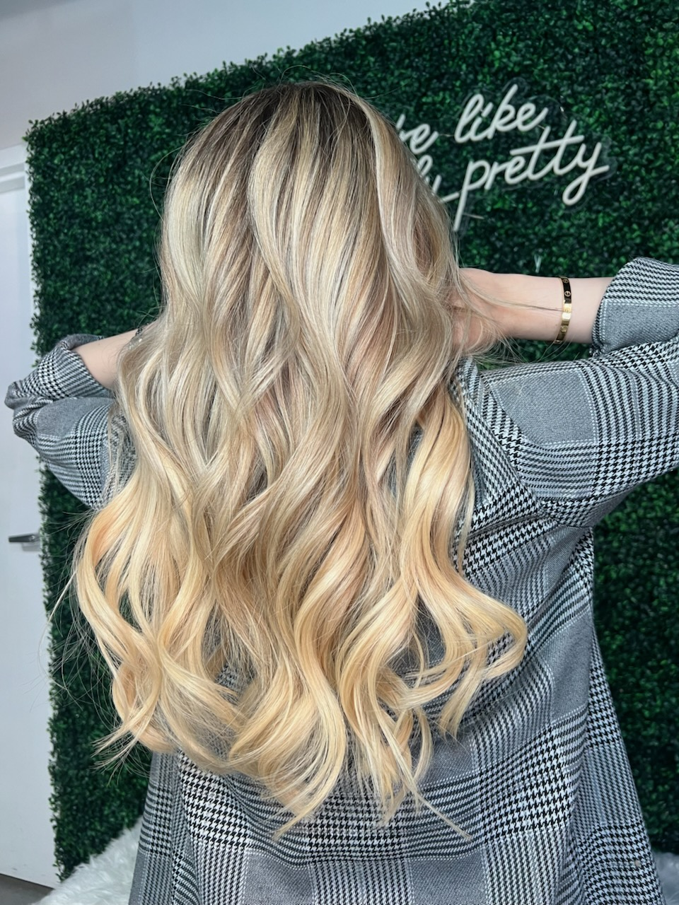 Woman with long wavy blonde hair facing a greenery wall with white script text.