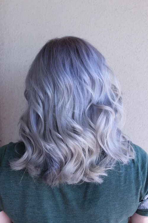 Back view of shoulder-length wavy silver-blonde hair against a plain beige wall