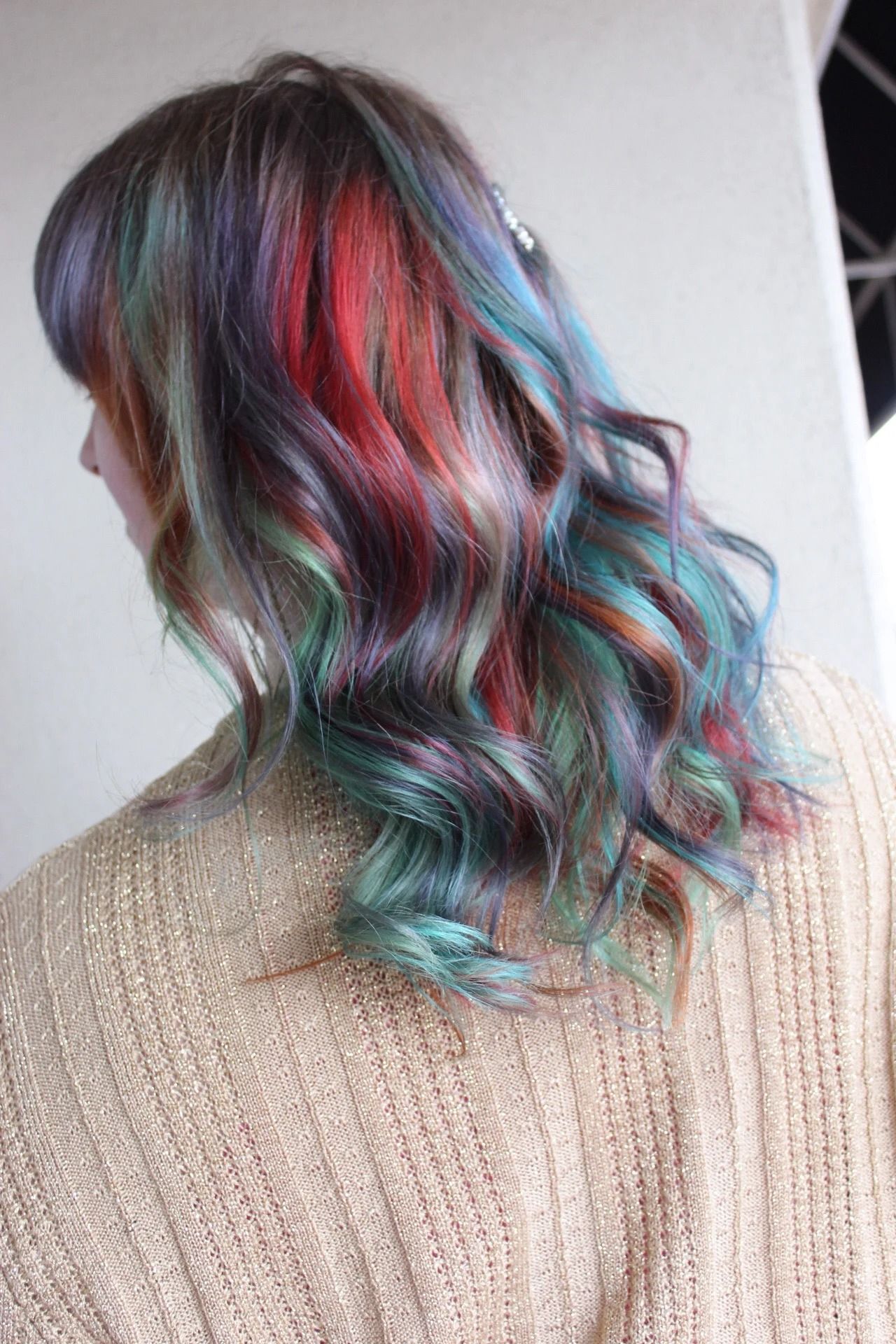 Wavy shoulder-length hair with teal, pink, and purple highlights against a beige sweater