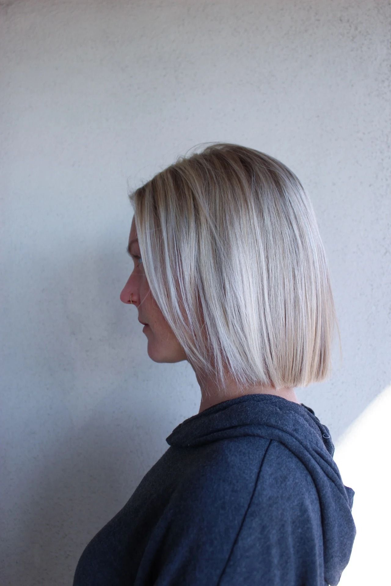 Side-profile of a person with blonde hair wearing a dark hoodie against a light wall