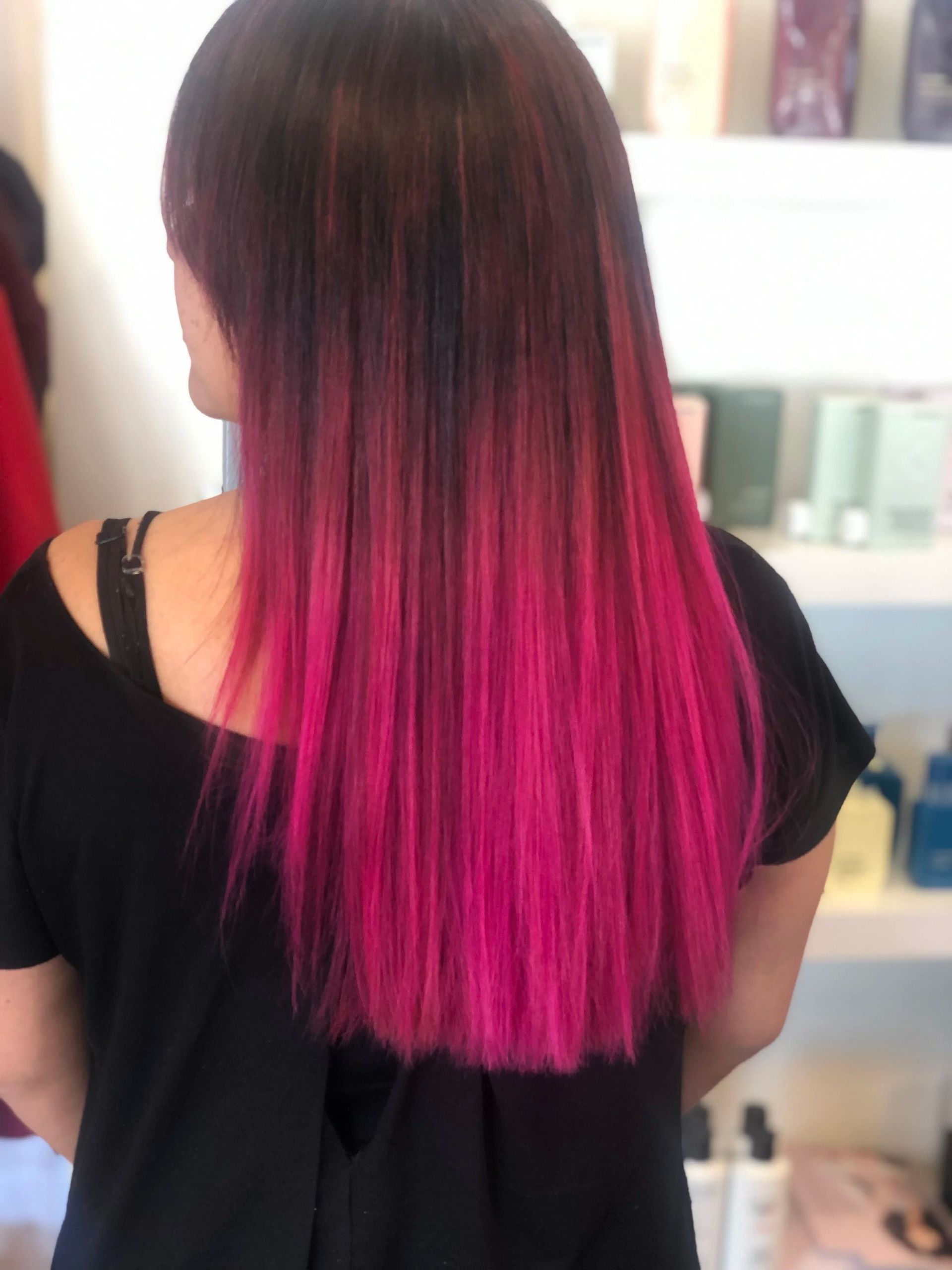 Person with straight dark hair fading to bright pink at the ends, seen from behind in a salon.