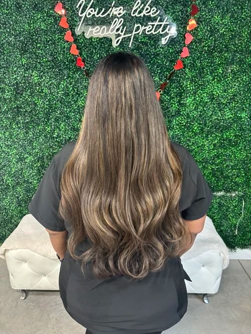 Back view of a person with long wavy brown hair standing before a green wall with a heart and “You’re like really pretty” sign