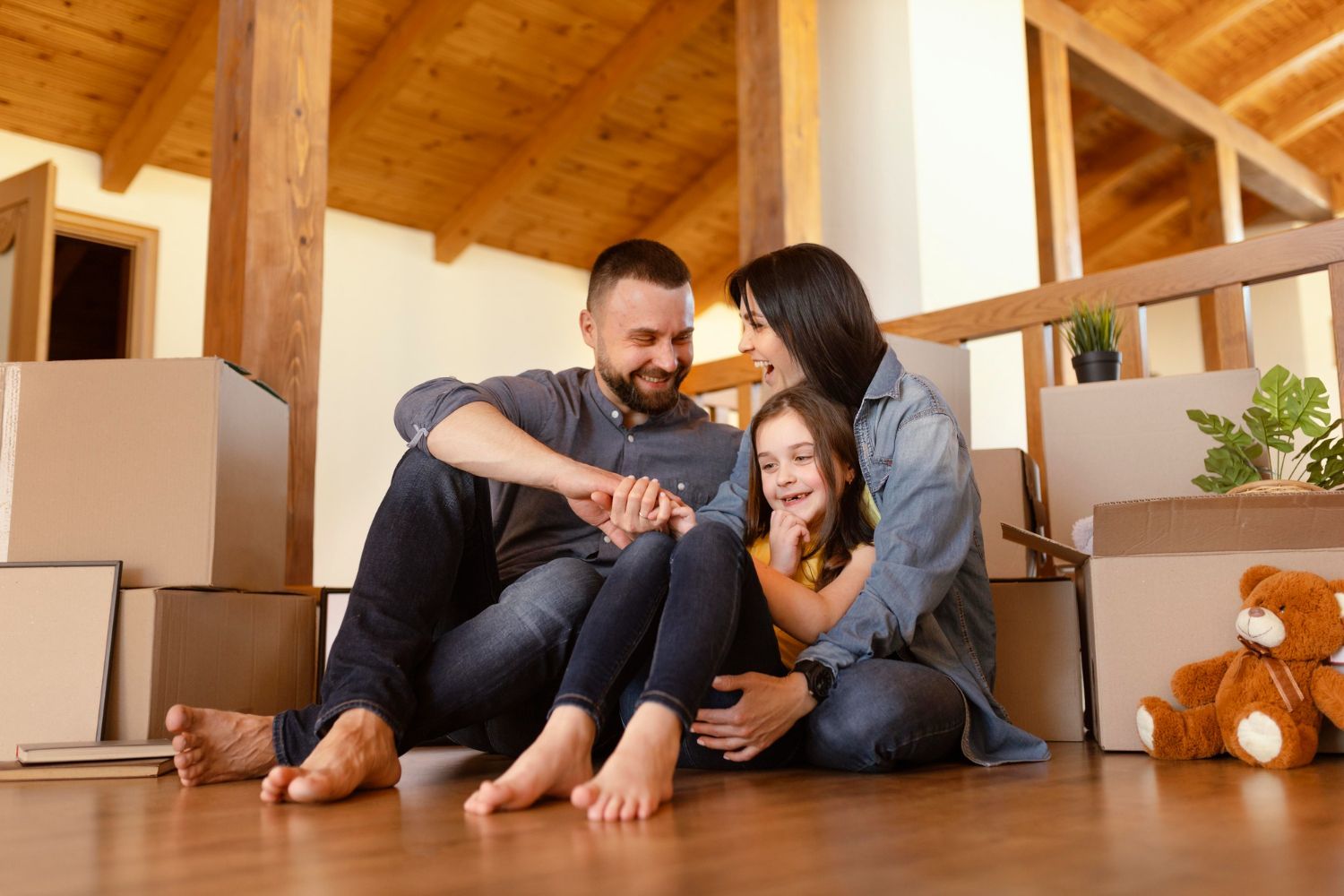 A family sitting on the floor together surrounded by cardboard moving boxes in a home with wooden architectural details.