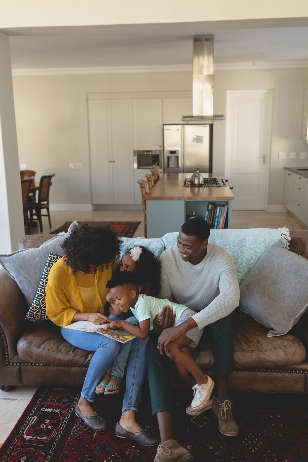 A family sits on a brown leather couch in a modern kitchen area, reading a book together.