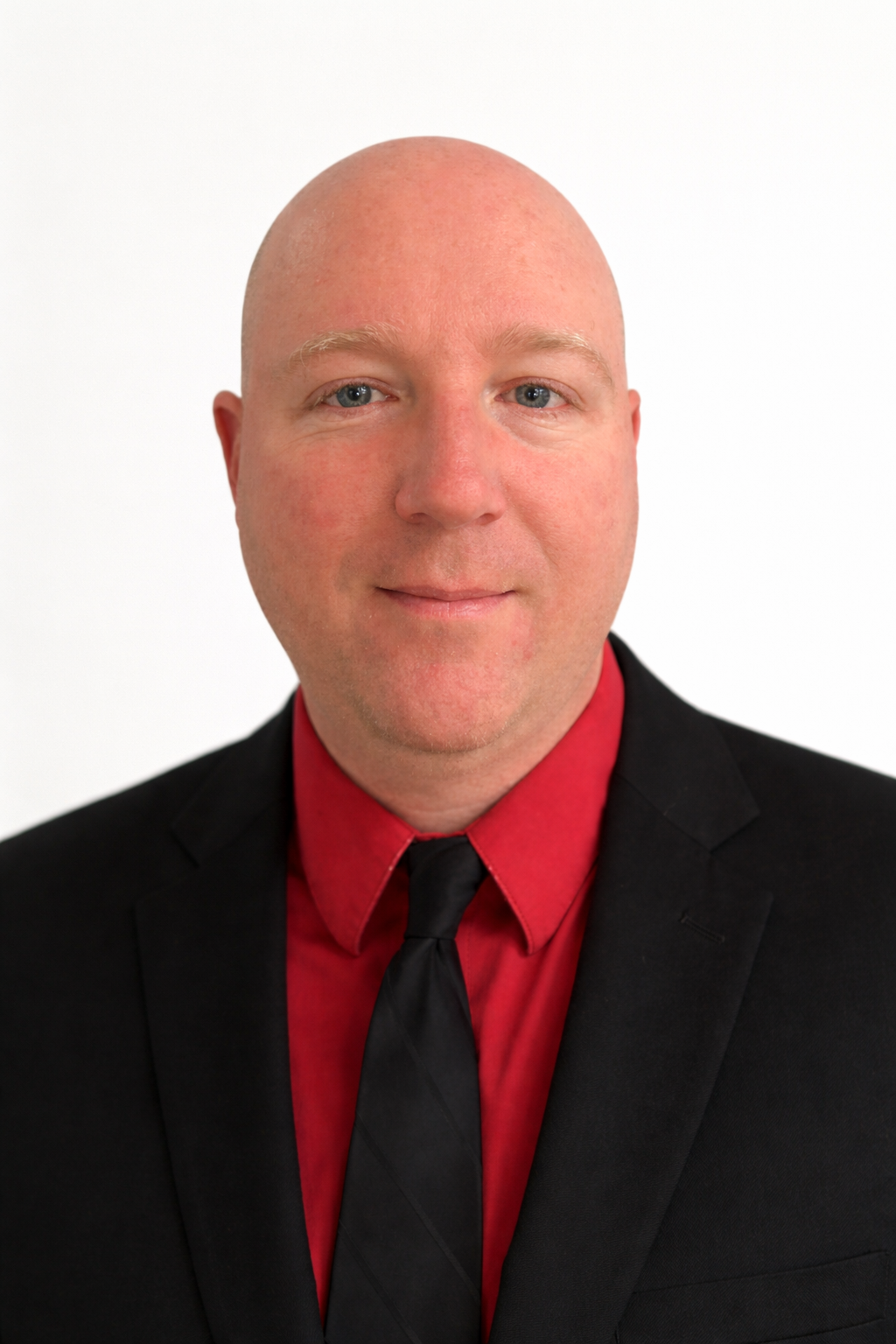 A person wearing a black suit, red shirt, and black necktie, posed against a plain white background.