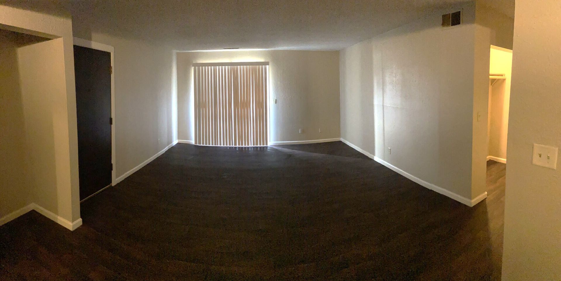 Empty living room with brown carpet, sliding door, and white walls.