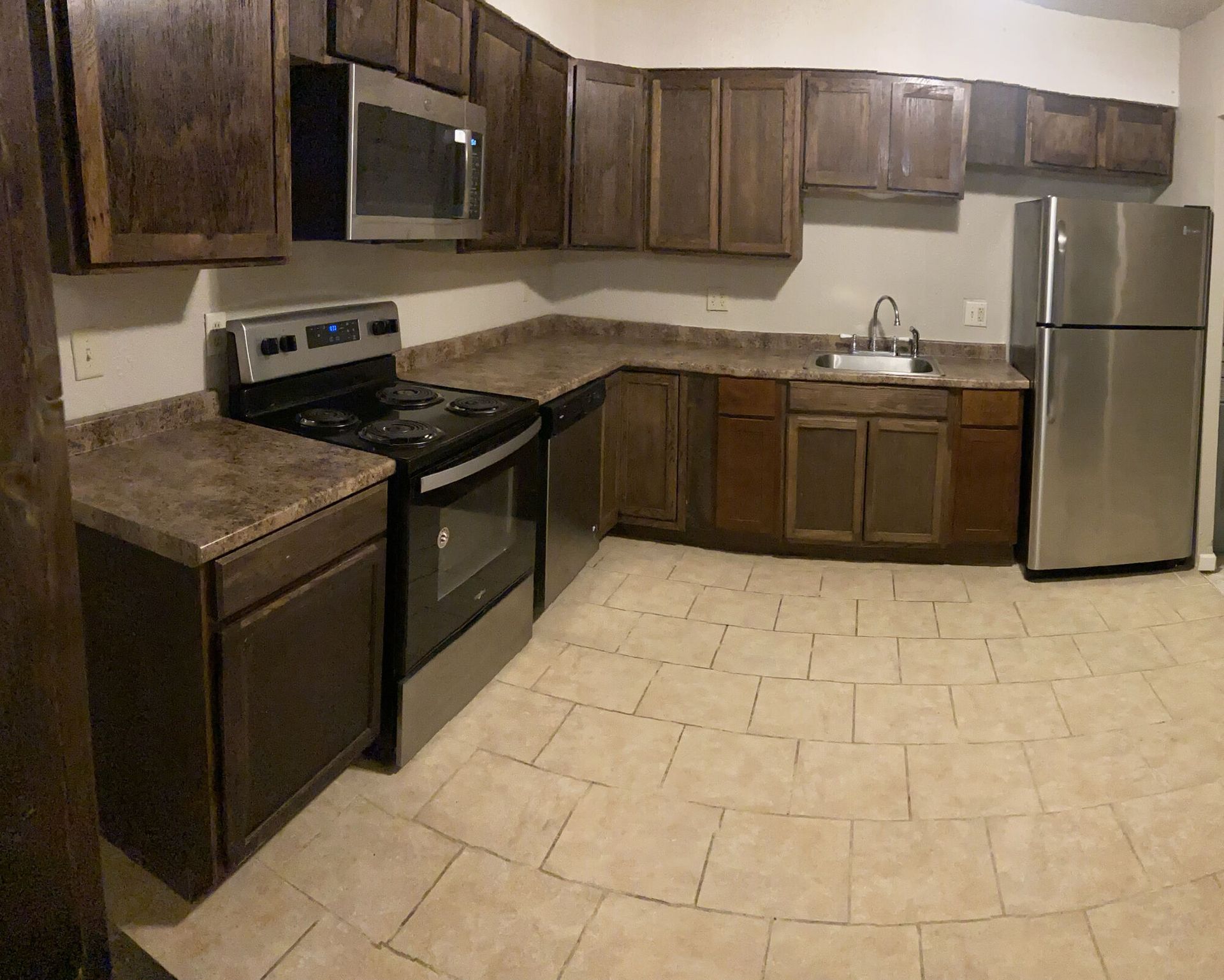 Kitchen with brown cabinets, stainless steel appliances, and beige tile floor.