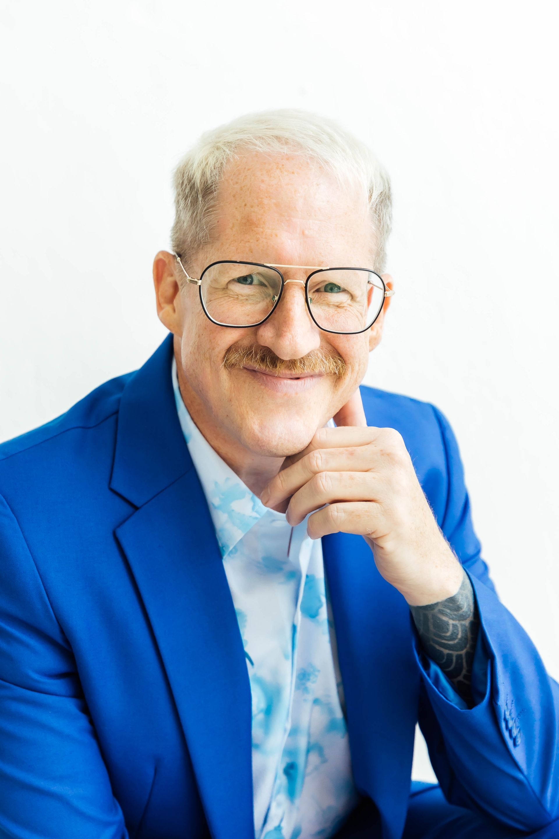 Man in blue suit holds hair dryer, smiling. White background.