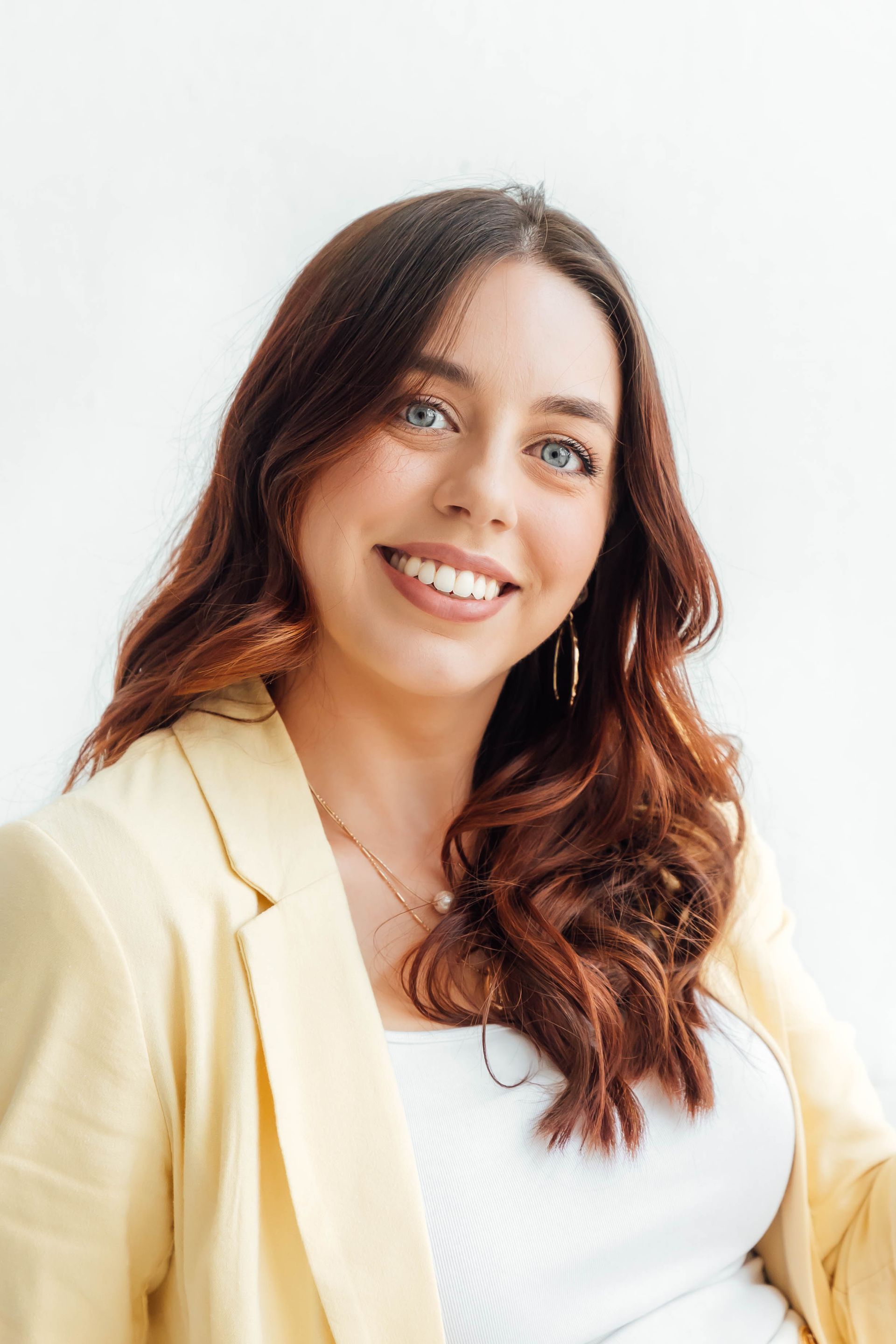 Woman in yellow blazer and white shorts, smiling, hand on hip against a white background.