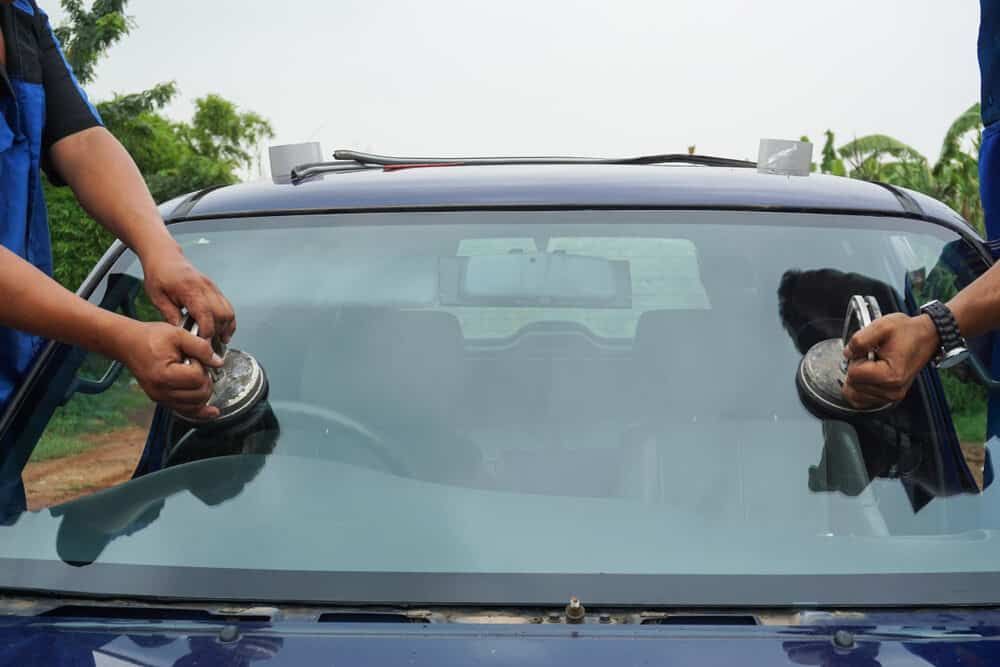 A Man is Installing a Windshield on a Blue Car — Shepparton Radiators & Windscreens in Mansfield, VIC