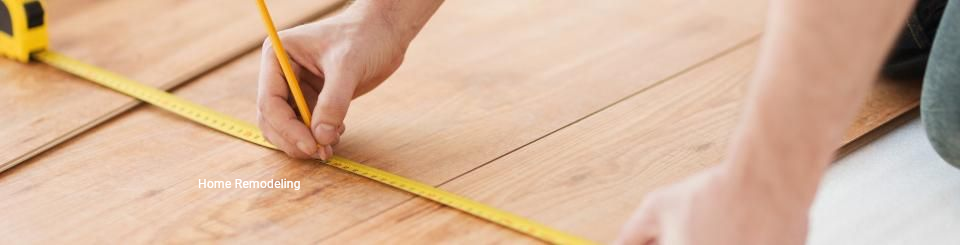 A close-up view of hands using a yellow tape measure and pencil to mark measurements on wooden flooring.