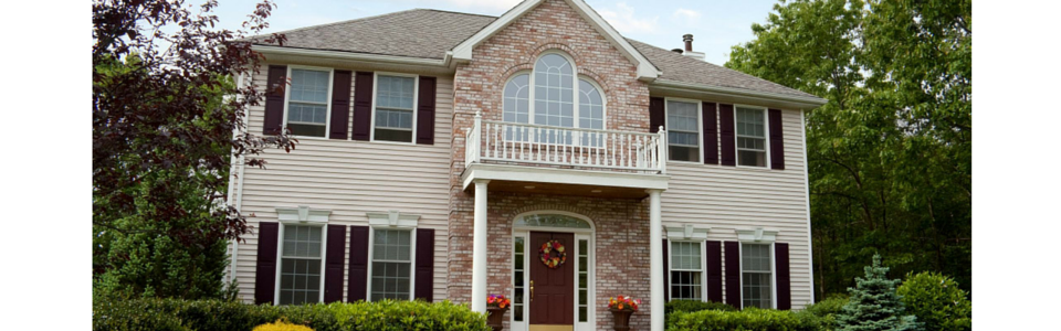 A two-story brick and siding house with dark shutters, a front porch, and a small balcony above the front door.