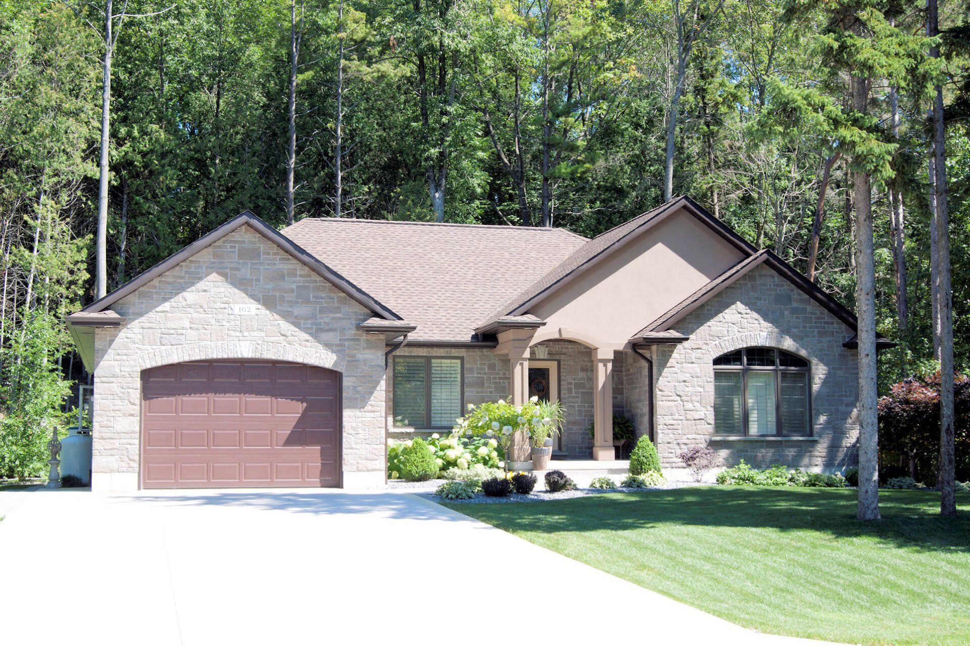 A brick house with a brown garage door is surrounded by trees