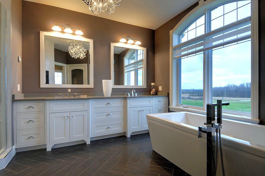 A bathroom with two sinks , two mirrors , a tub and a large window.
