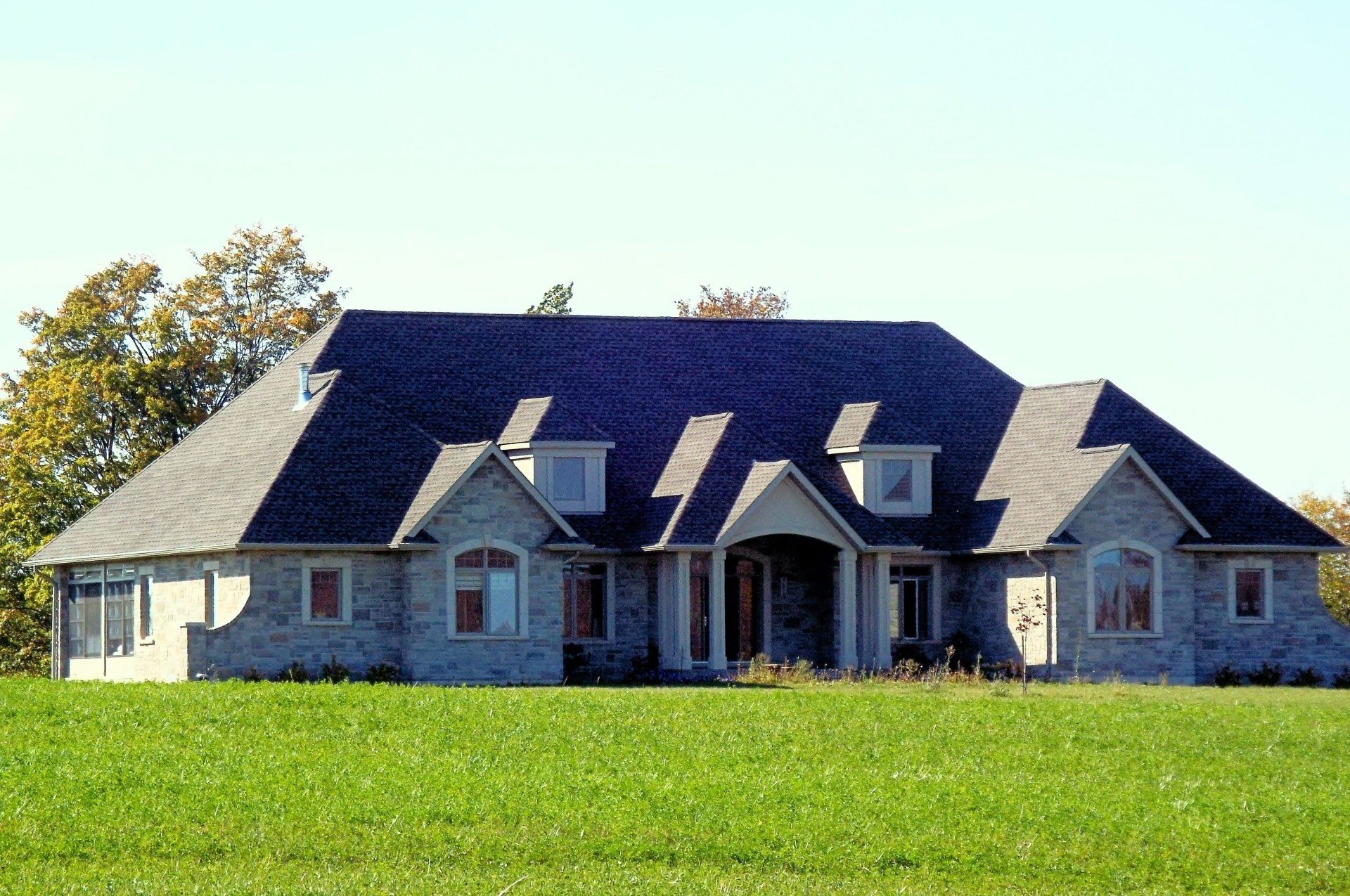 A large house with a blue roof is sitting in the middle of a grassy field.