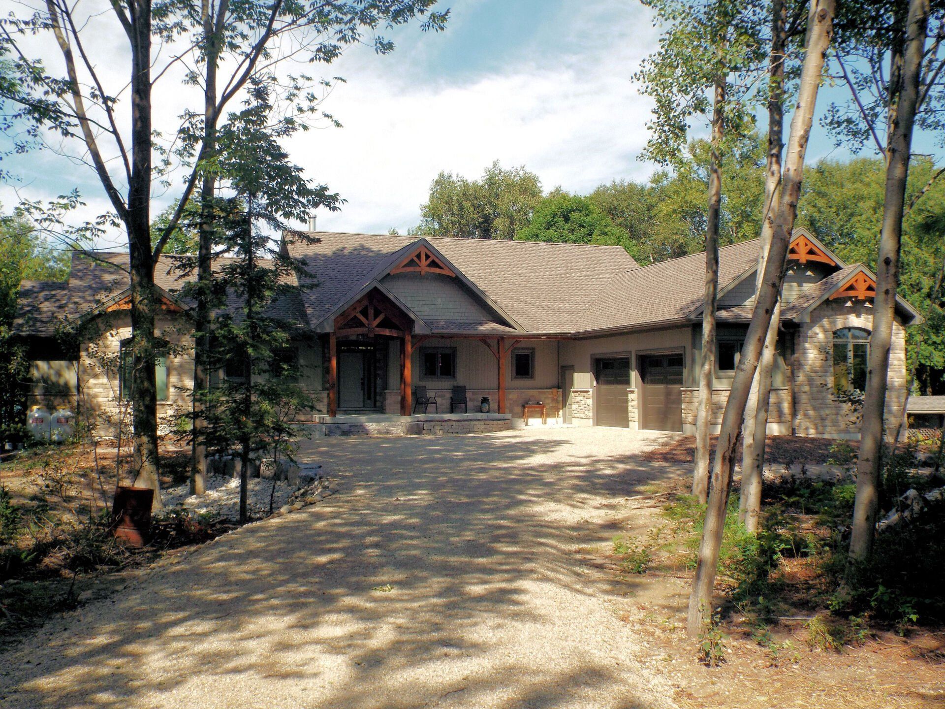 A large house is surrounded by trees and a gravel driveway