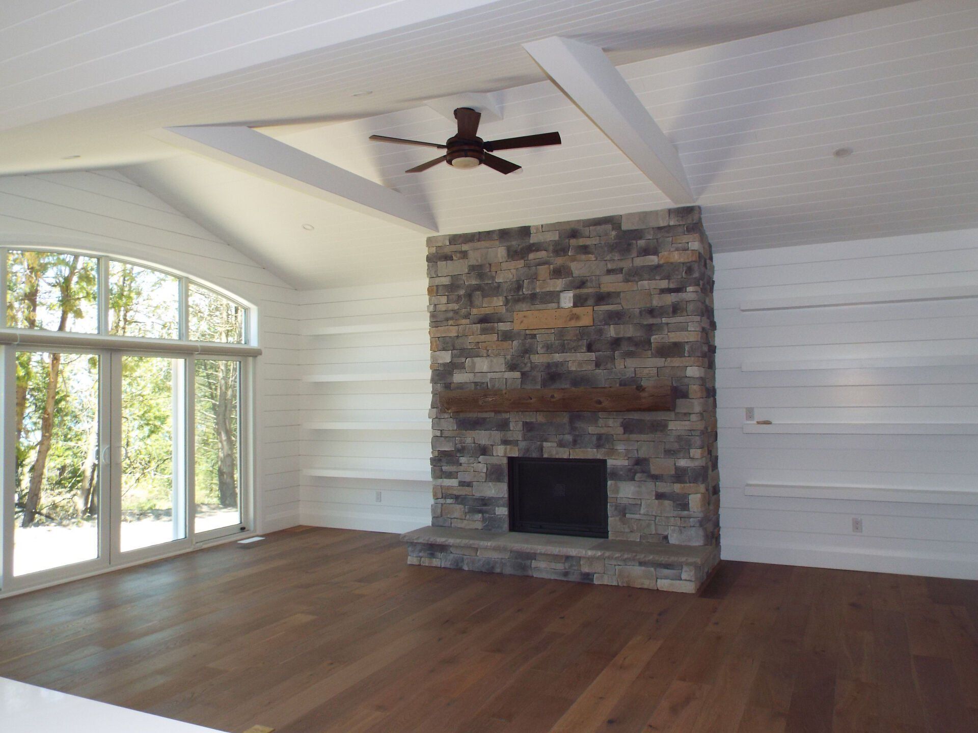 A living room with a stone fireplace and a ceiling fan