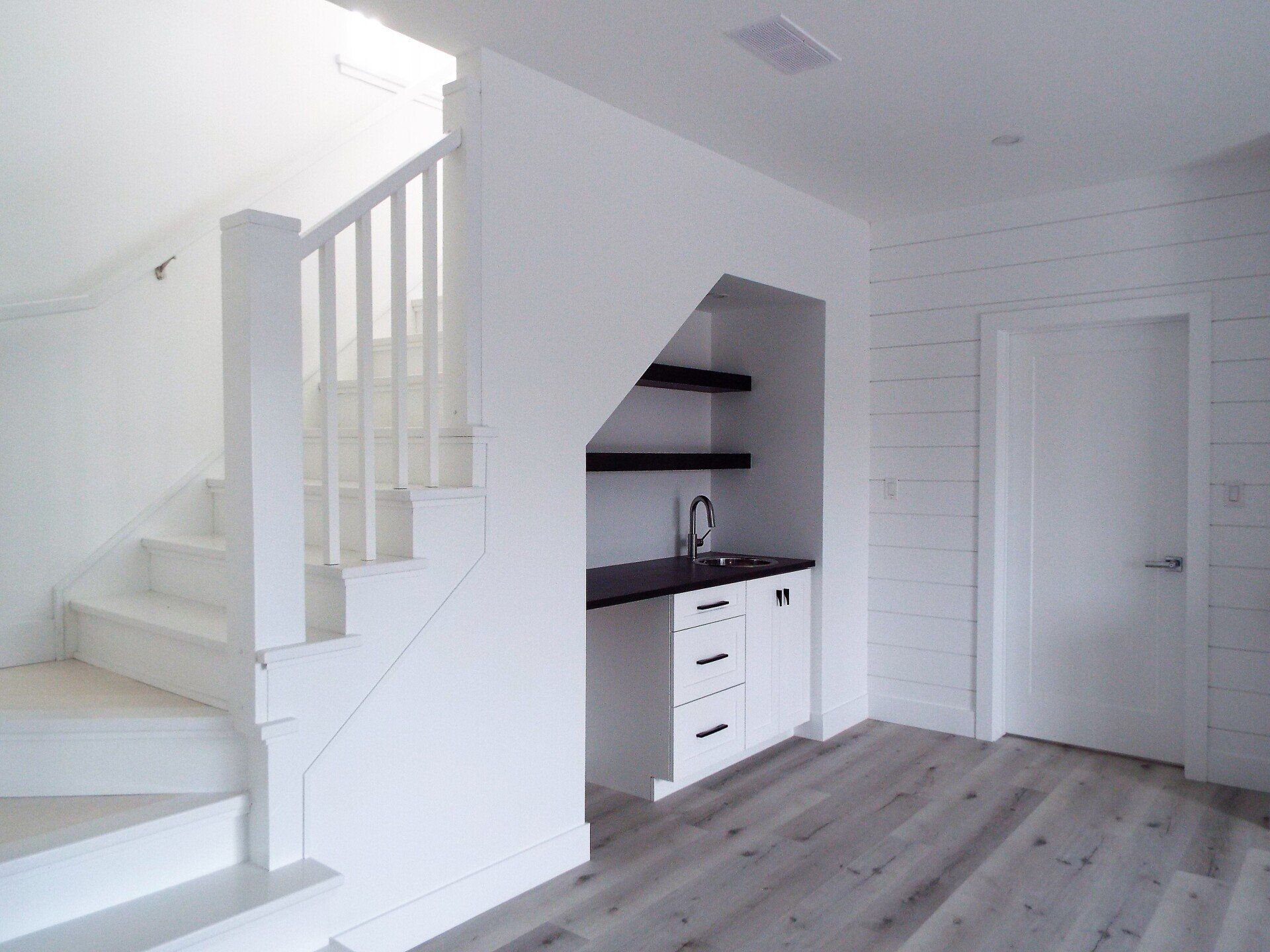 An empty room with stairs and a sink under the stairs