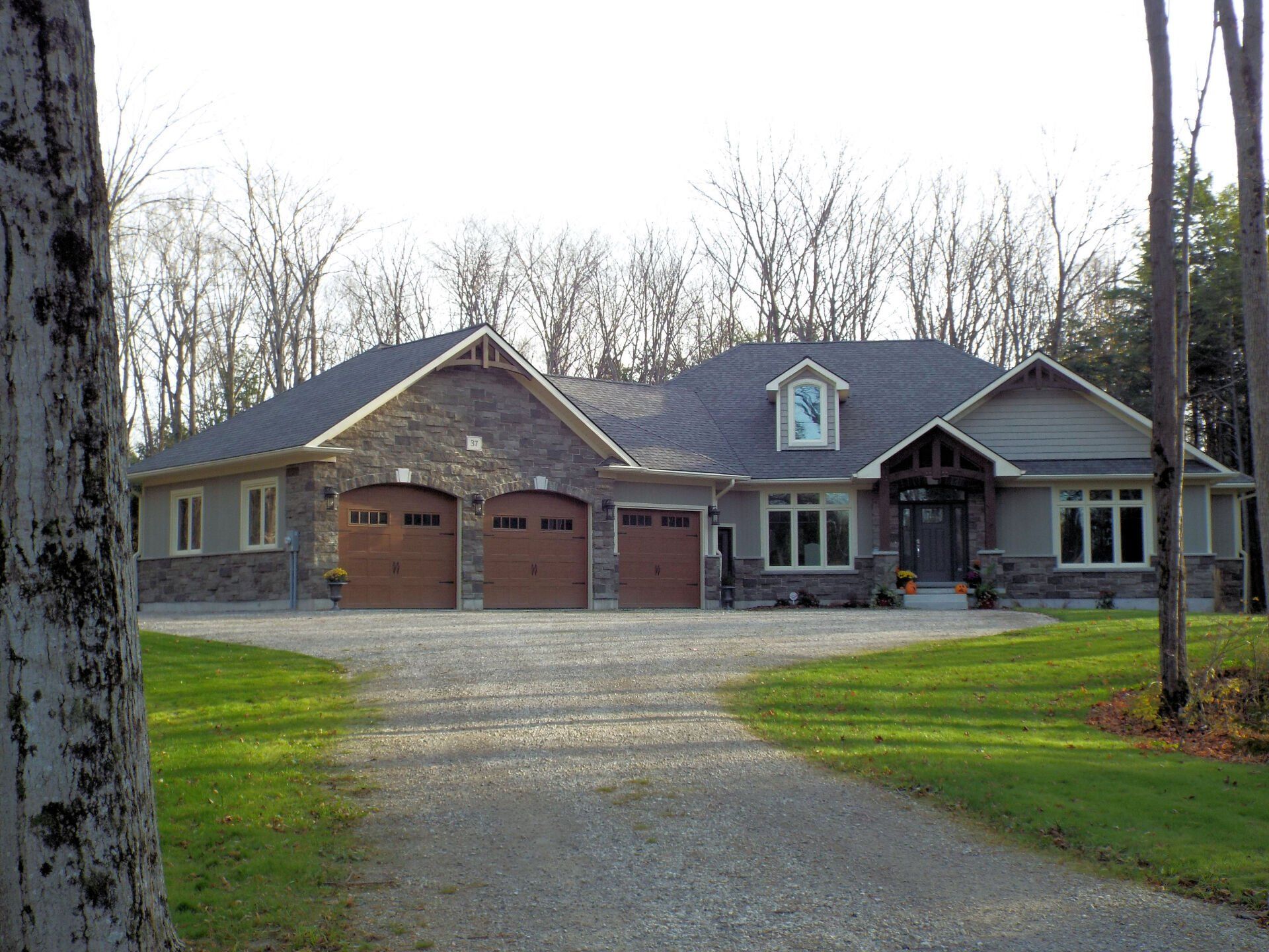 A large house with three garage doors is surrounded by trees