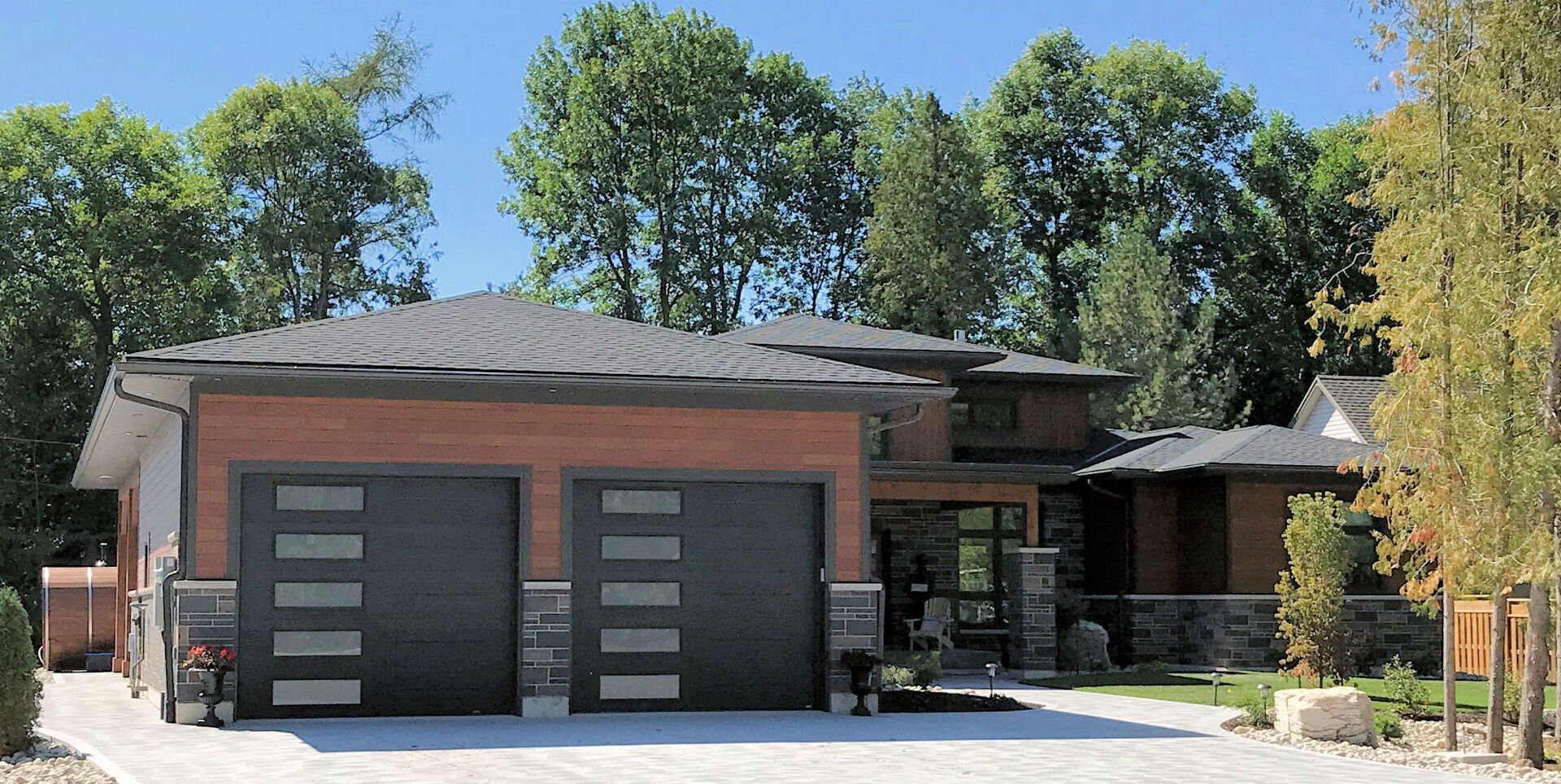 A large brick house with two garage doors is surrounded by trees.