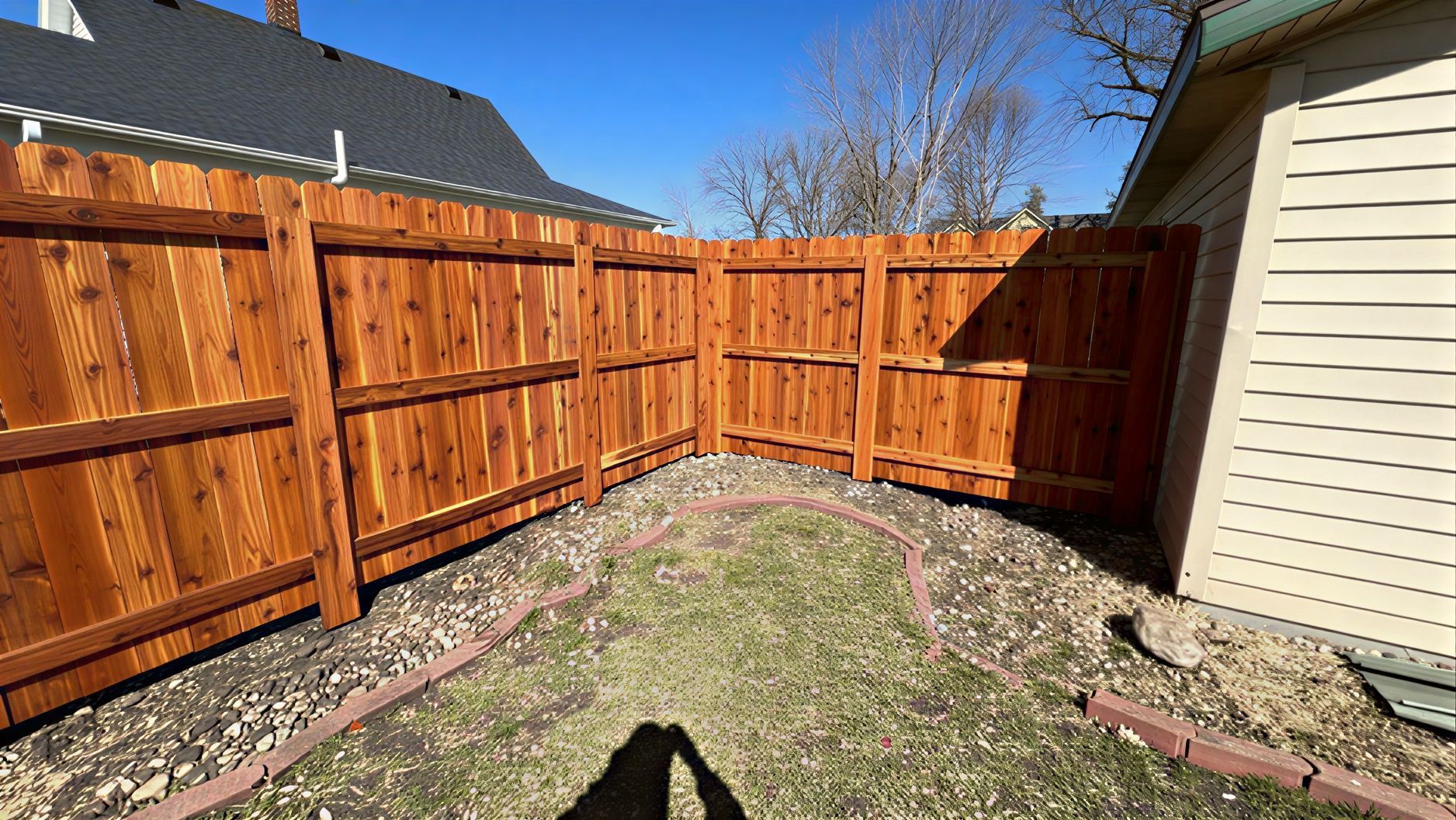 Sunny backyard corner with new wooden fencing and a small grass and rock border.