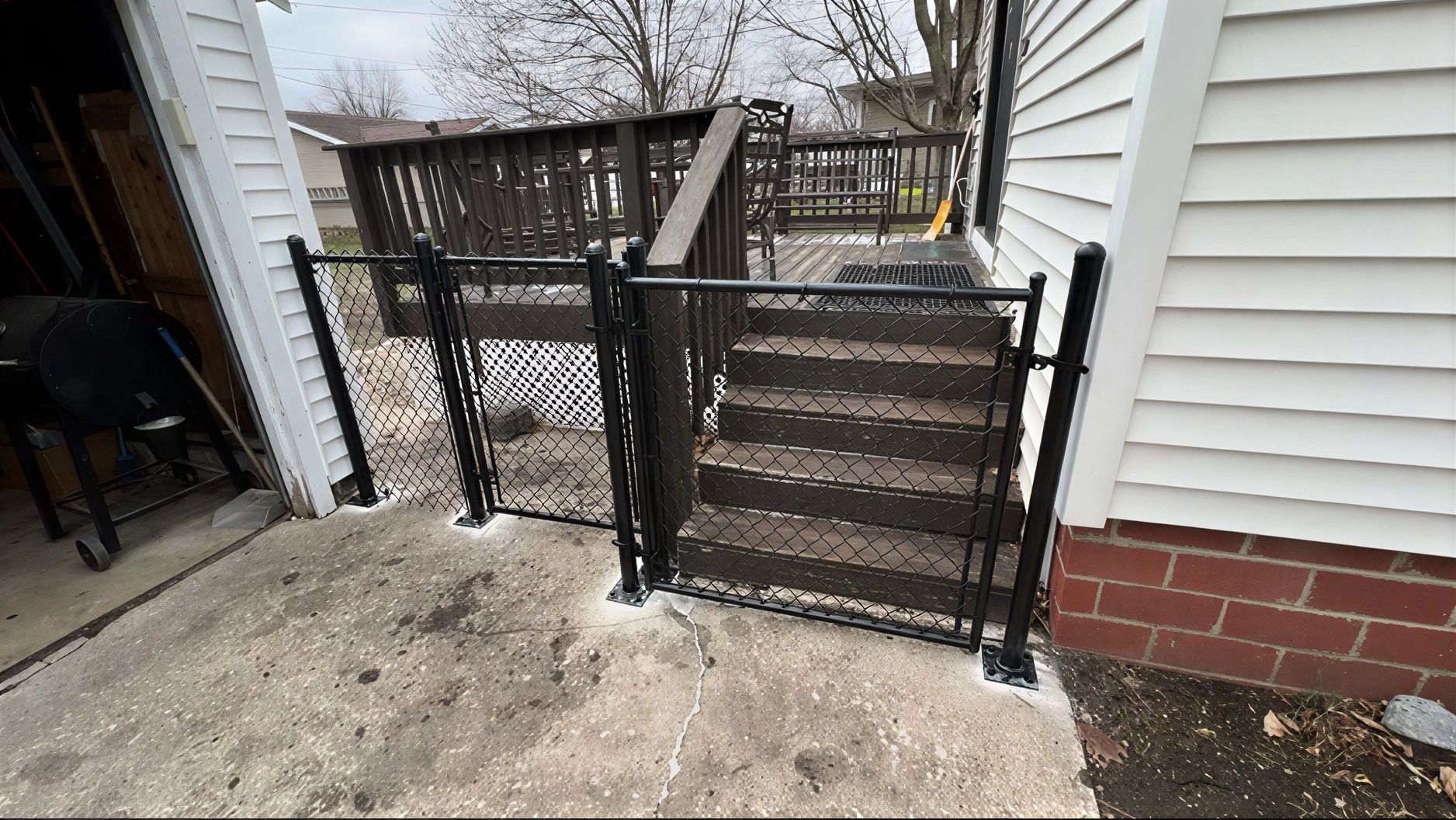 Black chain-link gate blocking access to wooden deck stairs beside a house.