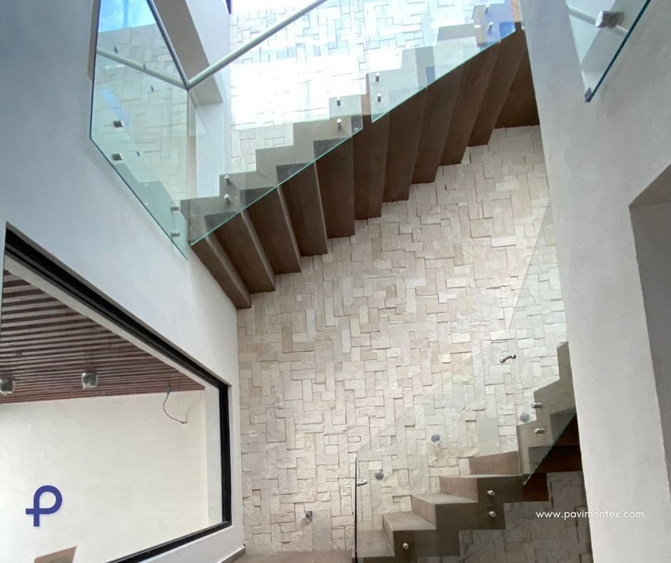 Escalera con barandilla de cristal y pared de piedra clara. Peldaños de madera marrón. Fotografía interior.
