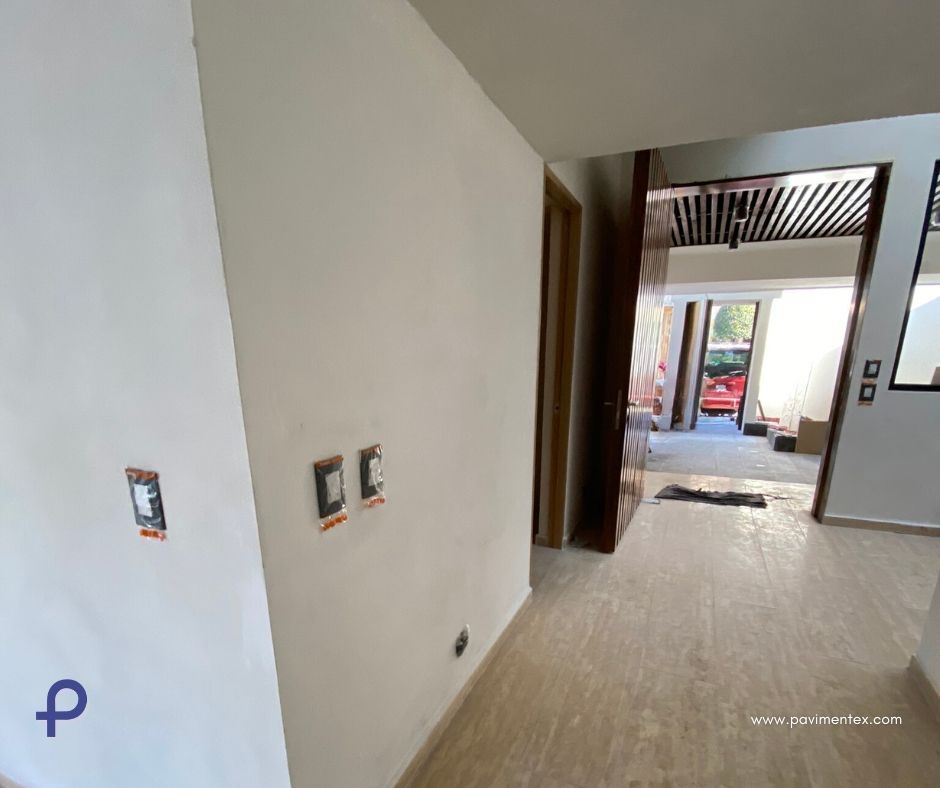 Pasillo interior con paredes sin terminar, enchufes eléctricos y puerta abierta a un área iluminada por el sol.