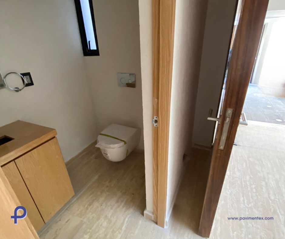 Interior de baño con inodoro, lavabo y puerta. Combinación de colores beige y marrón.