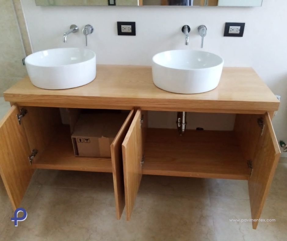 Mueble de baño con dos lavabos blancos, mueble de madera clara, puertas abiertas y caja en su interior.
