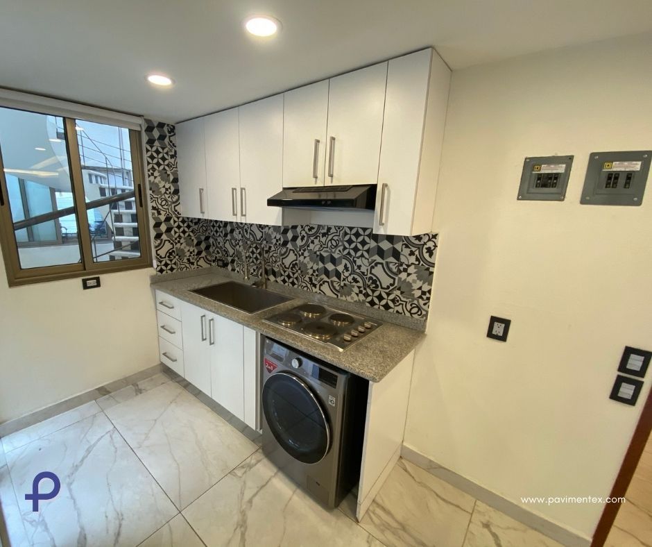 Una cocina con gabinetes blancos, estufa, lavadora y secadora, y una ventana.