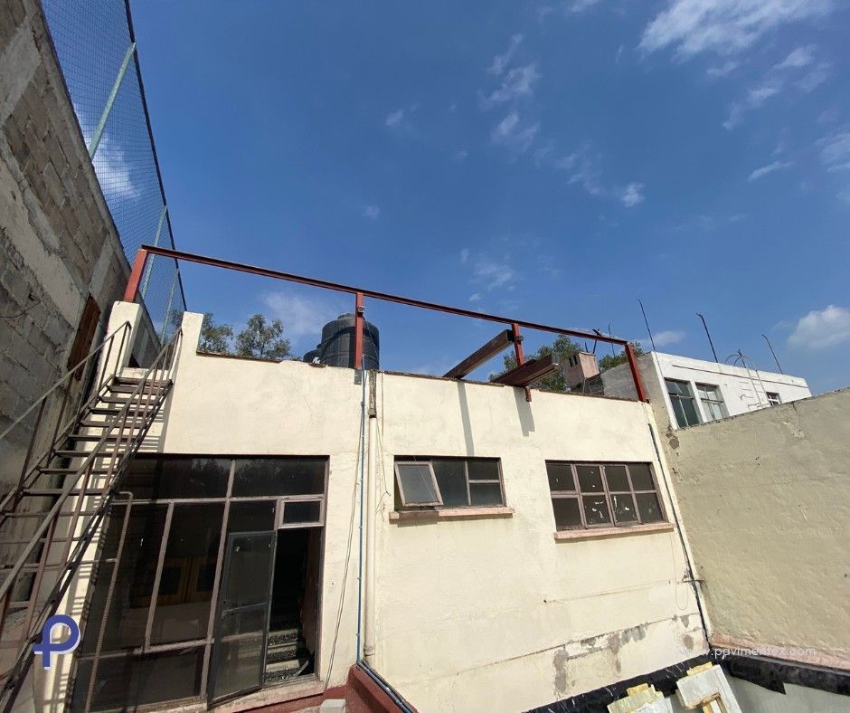 Un edificio de varios pisos con una escalera de metal negra y un tanque de agua en la azotea contra un cielo azul.
