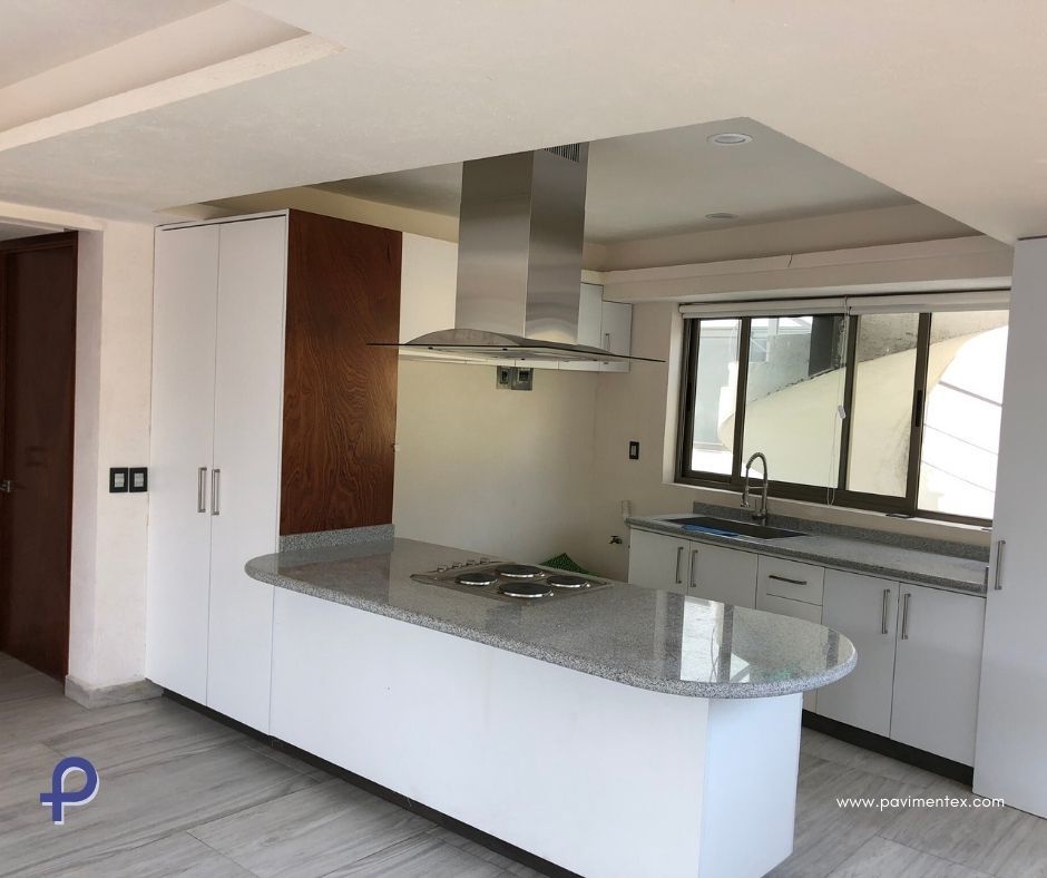 Una cocina con gabinetes blancos, sobres de granito y campana de acero inoxidable.