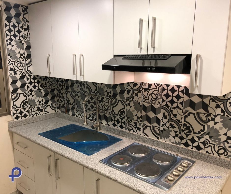 Una cocina con gabinetes blancos, horno de anafe, fregadero y campana.