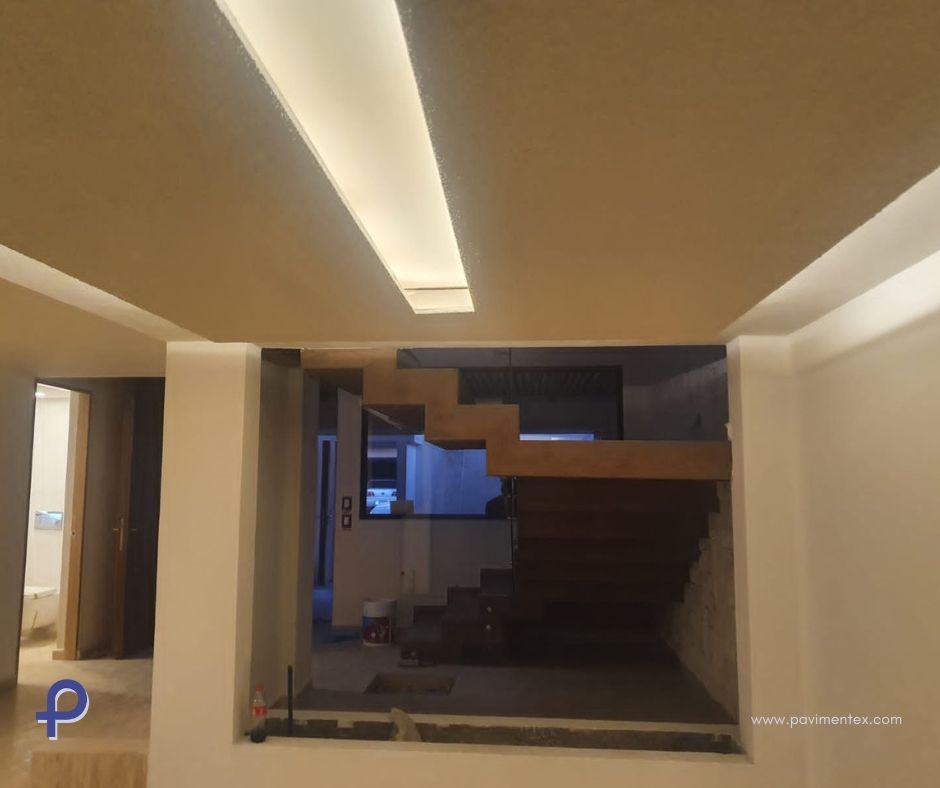 Vista interior con escaleras, una puerta y luces empotradas en el techo.