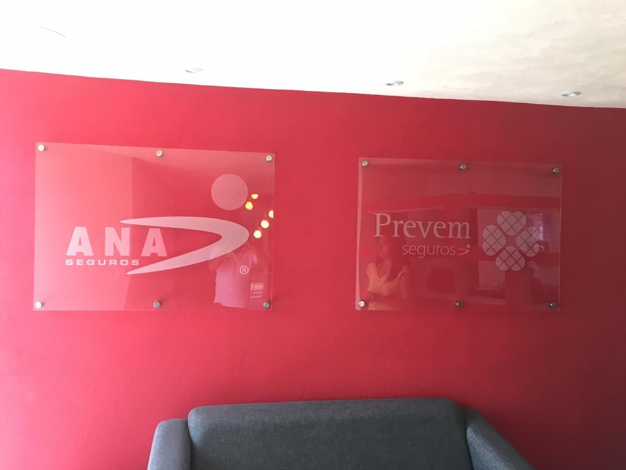 Dos carteles de cristal sobre una pared roja: “ANA Seguros” a la izquierda y “Prevem Seguros” a la derecha.