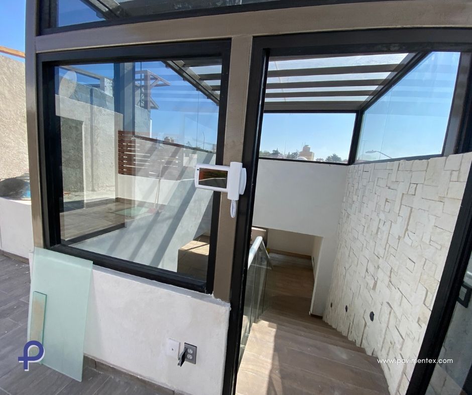 Escalera y rellano con paredes de cristal. Vista exterior con la puerta abierta. Luz solar intensa.