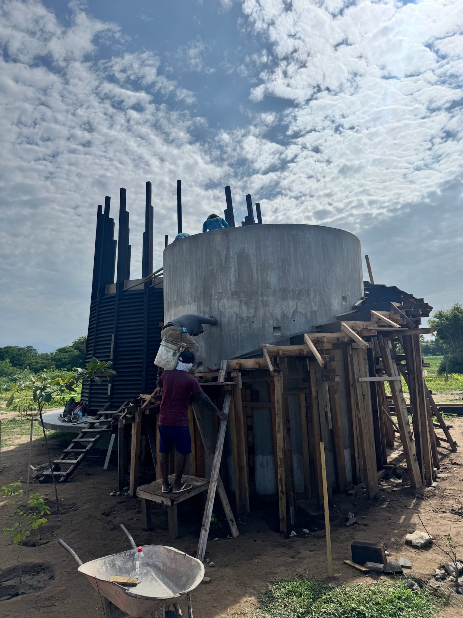 Construcción de una torre de agua de hormigón con soportes de madera; trabajador en escalera.