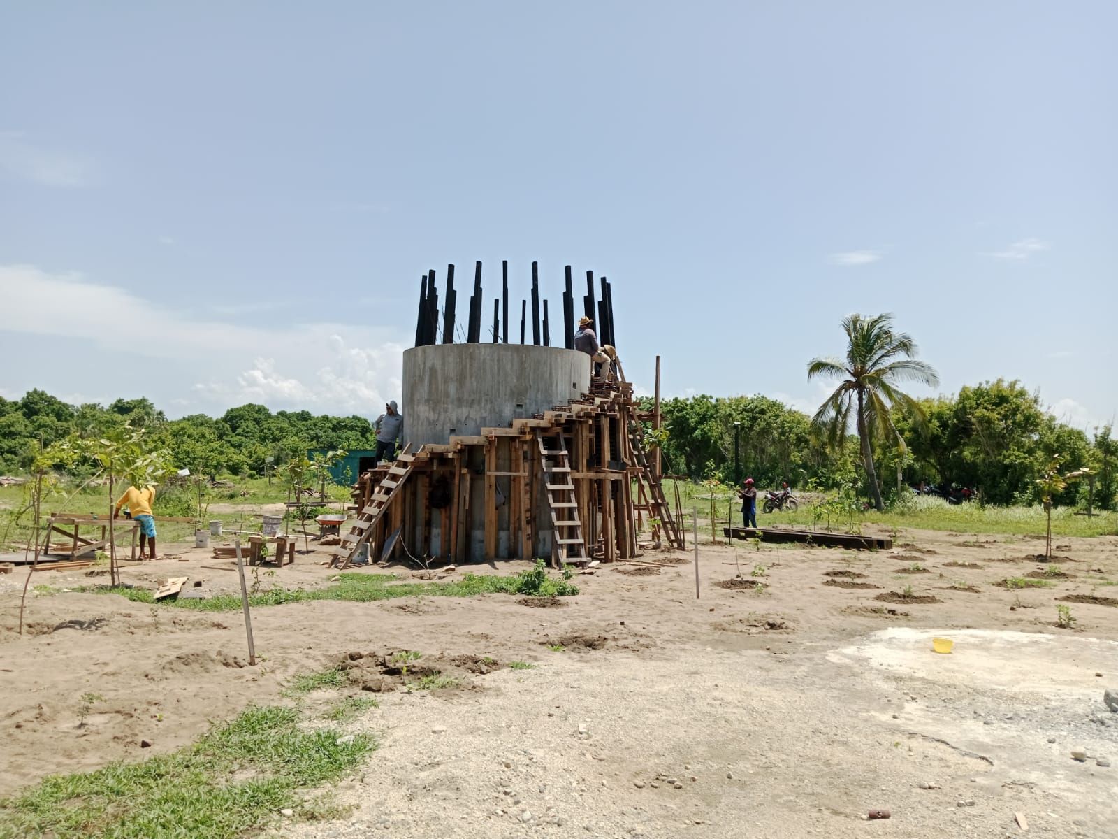 Obra con estructura de hormigón y andamios de madera. Dos trabajadores están presentes en el exterior.