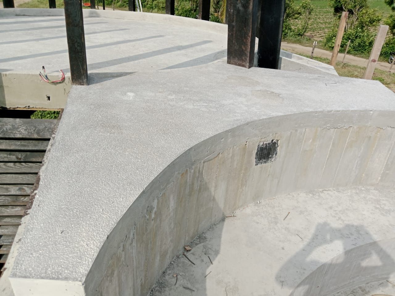 Estructura de hormigón con canto curvo, superficie gris, rodeada de valla de madera y pilares.