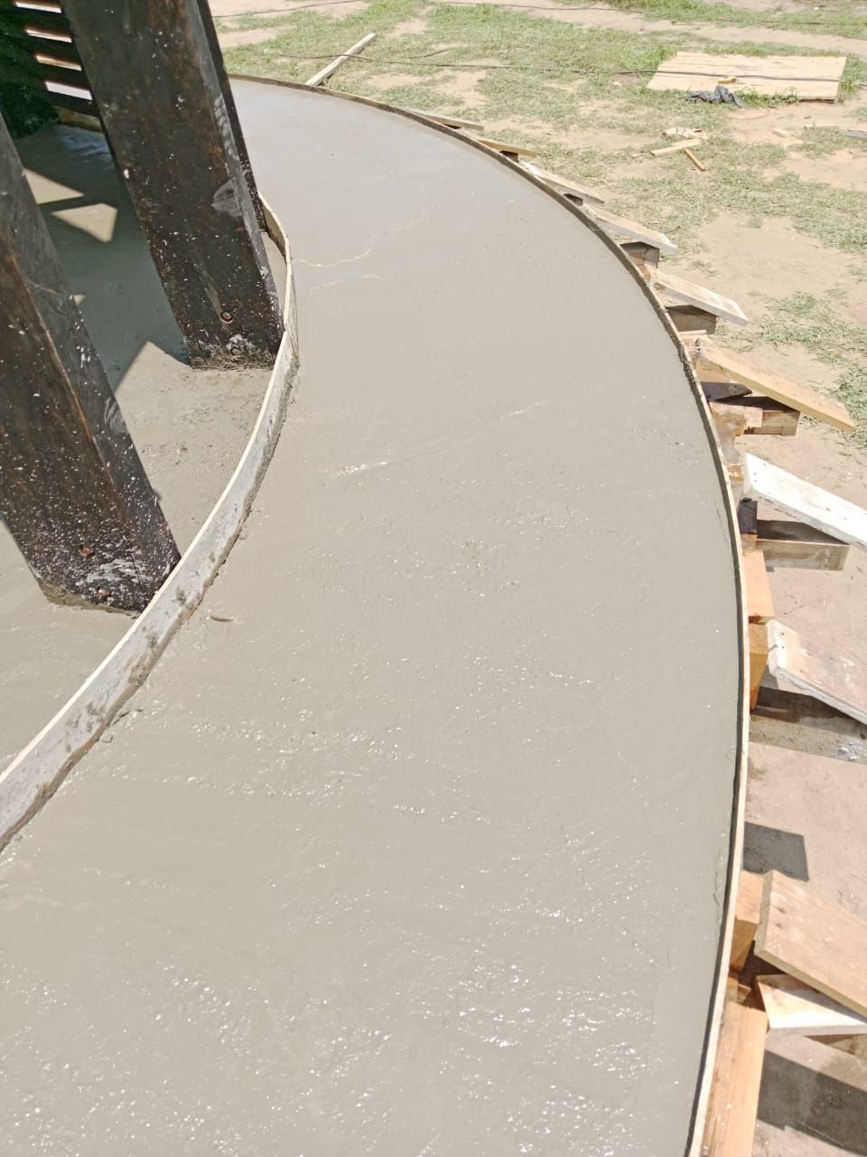 Hormigón recién vertido en forma curva, rodeado de soportes y postes de madera.